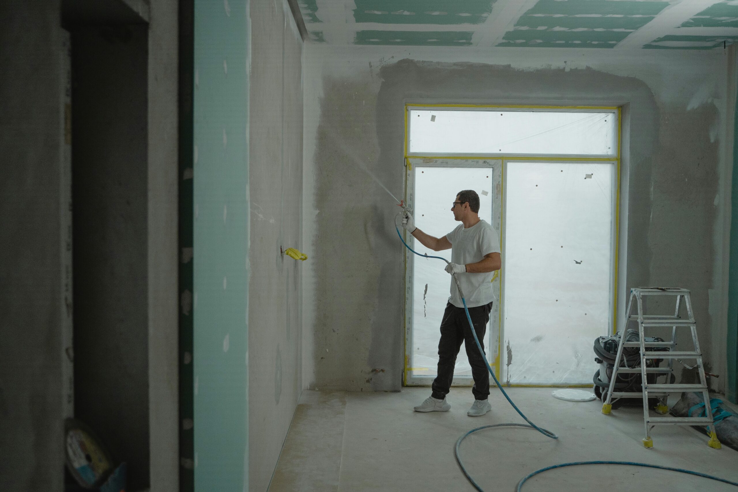 A man sprays paint on a wall while renovating an indoor room with professional equipment.